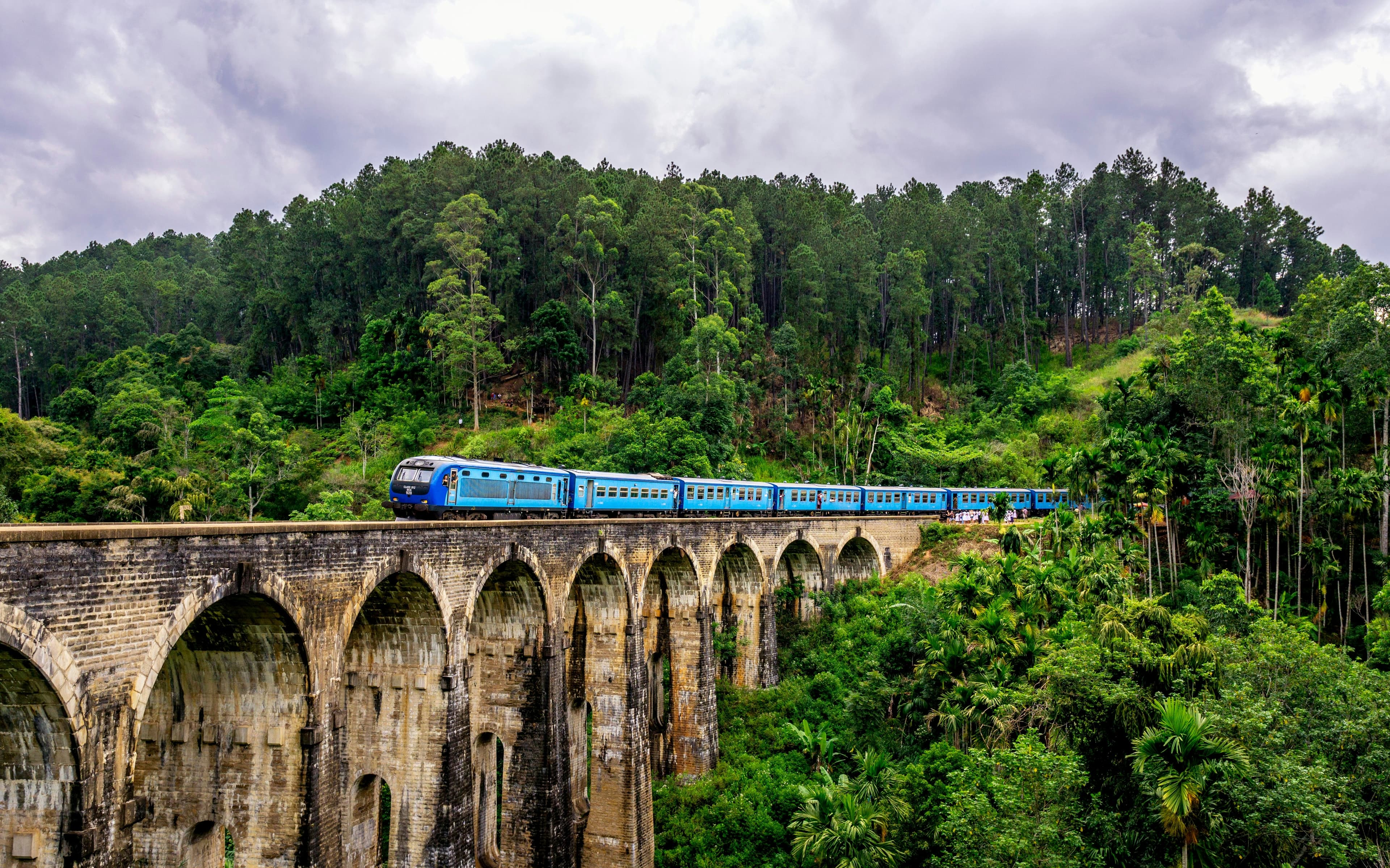 A blue train crossing the Nine Arches Bridge near Ella, surrounded by forest